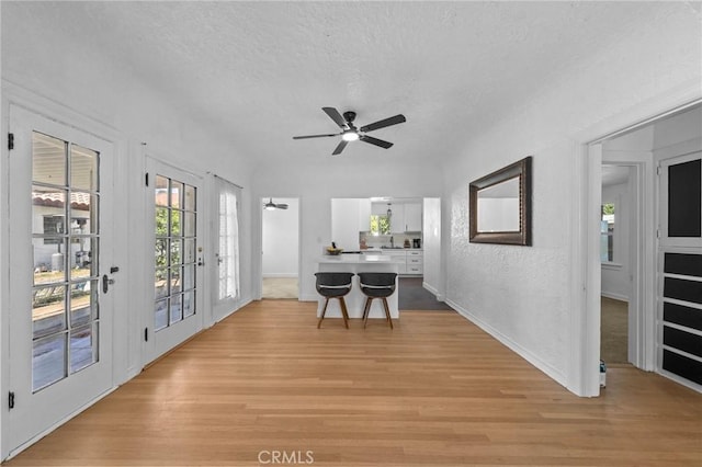 dining room with a ceiling fan, light wood-type flooring, a textured ceiling, and baseboards