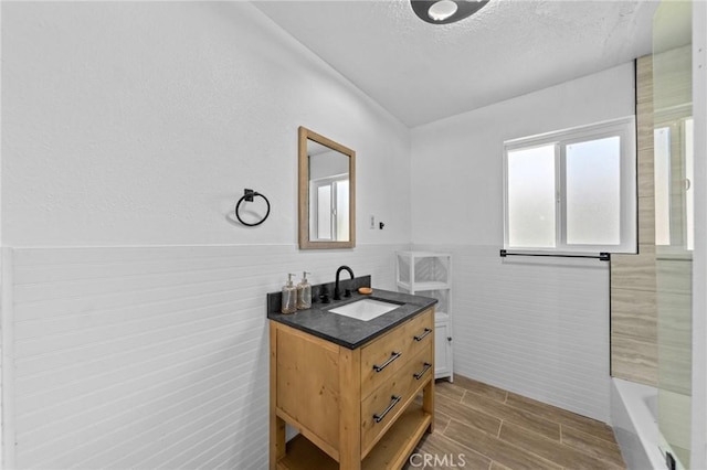 bathroom with wainscoting, a bathing tub, wood tiled floor, a textured ceiling, and vanity