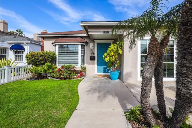 entrance to property with a yard, fence, and stucco siding