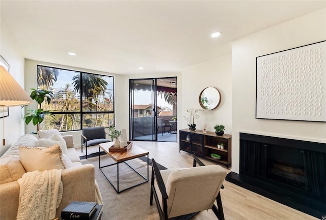 living area featuring light wood-style flooring, a fireplace with raised hearth, and recessed lighting