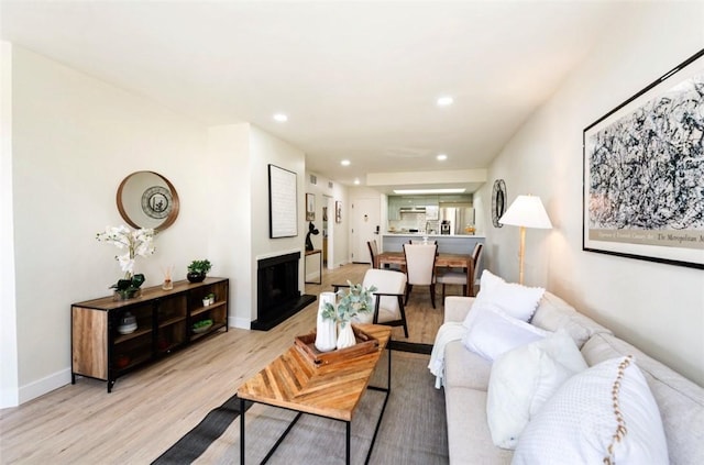 living area with recessed lighting, baseboards, a fireplace with raised hearth, and light wood finished floors