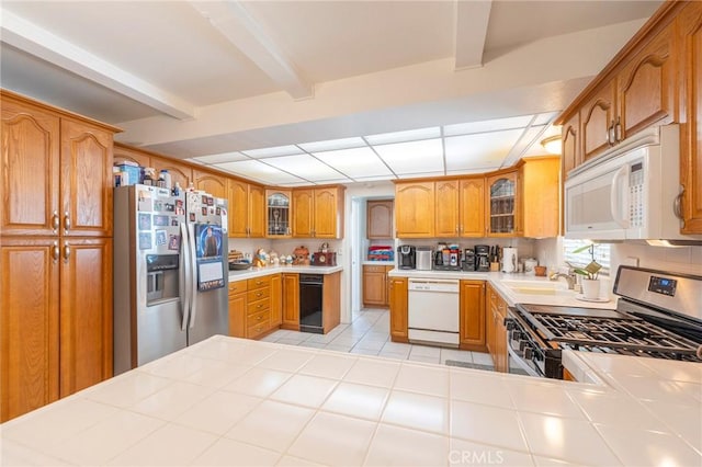 kitchen featuring beam ceiling, appliances with stainless steel finishes, glass insert cabinets, light tile patterned flooring, and a sink