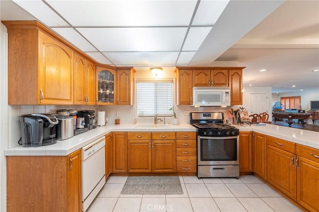 kitchen with white appliances, light tile patterned floors, glass insert cabinets, and brown cabinets