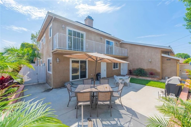 rear view of property with a balcony, a gate, fence, and stucco siding