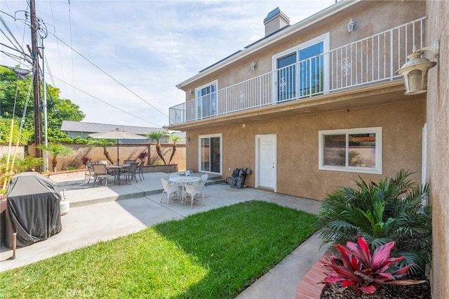 rear view of house featuring a yard, fence, a balcony, and stucco siding