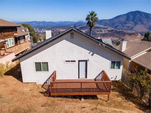 rear view of house with a deck with mountain view, a chimney, and stucco siding