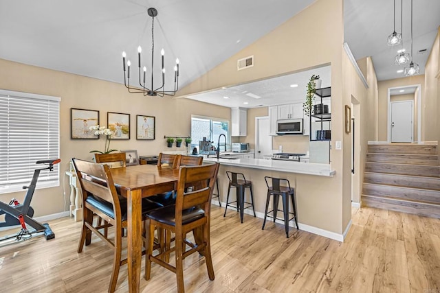 dining area featuring visible vents, lofted ceiling, an inviting chandelier, stairs, and light wood-style floors