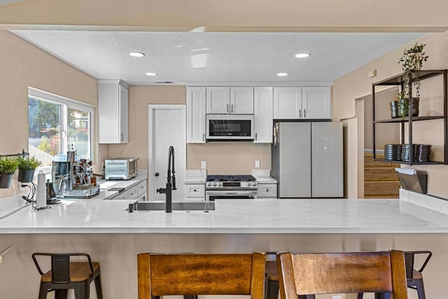 kitchen featuring stainless steel gas stove, freestanding refrigerator, a peninsula, a sink, and recessed lighting