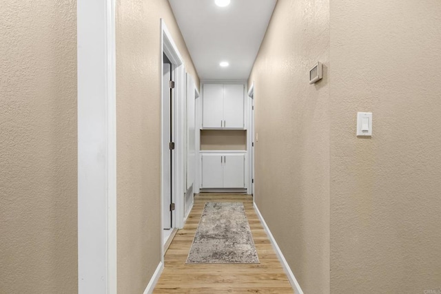 hallway featuring recessed lighting, baseboards, a textured wall, and light wood finished floors