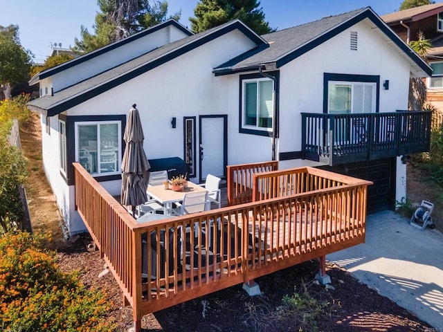 rear view of property with driveway, an attached garage, a deck, and stucco siding