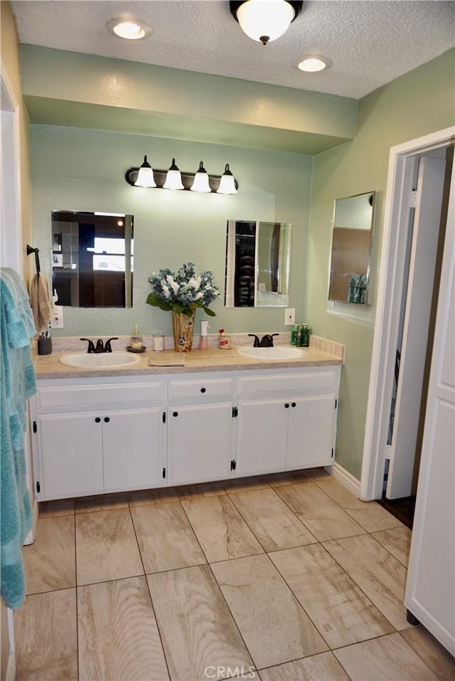 full bath featuring a textured ceiling, double vanity, a sink, and recessed lighting