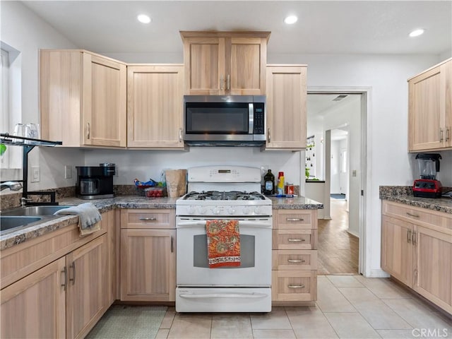 kitchen with stainless steel microwave, white gas stove, light brown cabinets, a sink, and recessed lighting