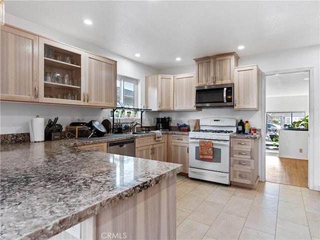 kitchen featuring dark stone counters, light brown cabinetry, appliances with stainless steel finishes, and glass insert cabinets