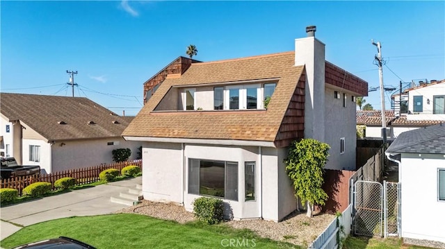 back of property featuring roof with shingles, a chimney, stucco siding, a lawn, and fence