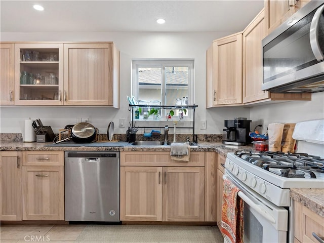 kitchen with recessed lighting, appliances with stainless steel finishes, glass insert cabinets, light brown cabinets, and a sink