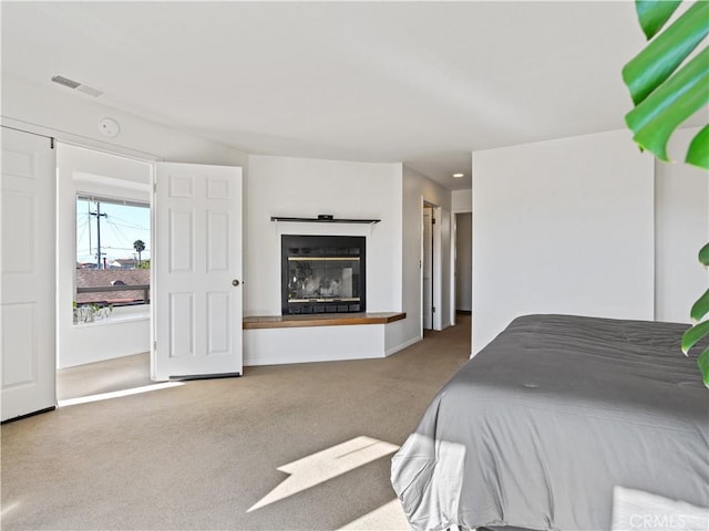 bedroom featuring carpet, a glass covered fireplace, visible vents, and baseboards