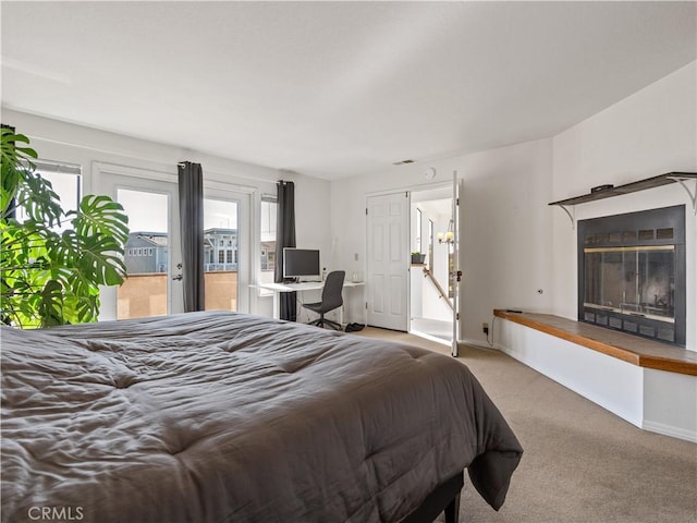 bedroom with access to outside, baseboards, a glass covered fireplace, and light colored carpet
