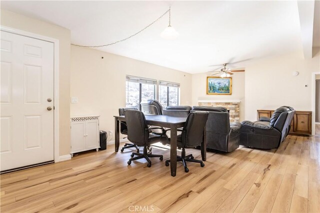 dining area with light wood-style floors, ceiling fan, and a fireplace