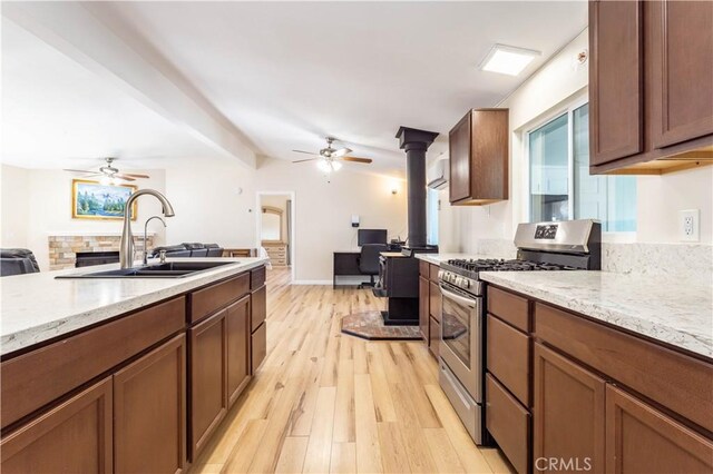 kitchen featuring light wood finished floors, stainless steel gas range oven, light stone counters, open floor plan, and a sink