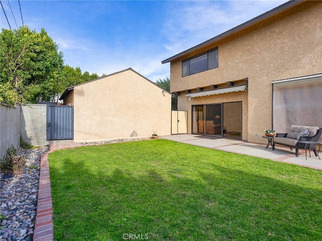 rear view of house featuring a patio, a yard, a gate, and stucco siding