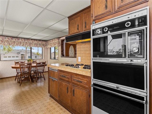 kitchen featuring double wall oven, light countertops, brown cabinets, light floors, and wallpapered walls