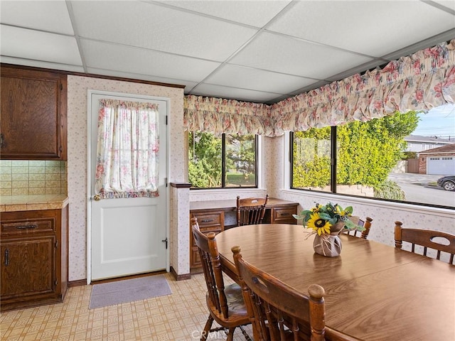 dining area featuring light floors, a paneled ceiling, and wallpapered walls