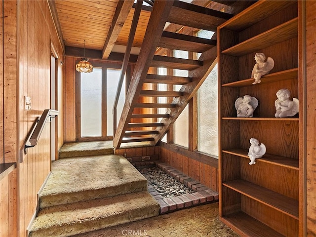 staircase featuring carpet floors, wooden ceiling, wood walls, and beamed ceiling