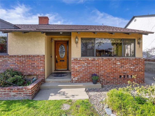 doorway to property featuring brick siding, a chimney, a shingled roof, and stucco siding