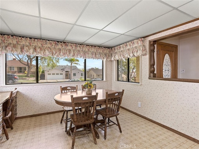 dining room with a paneled ceiling, baseboards, a residential view, light floors, and wallpapered walls