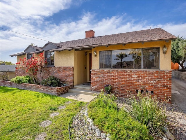 ranch-style house with brick siding, a chimney, stucco siding, a shingled roof, and a front lawn