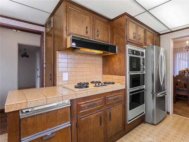 kitchen with under cabinet range hood, white gas stovetop, freestanding refrigerator, light floors, and wallpapered walls