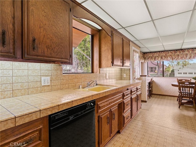 kitchen featuring a paneled ceiling, a sink, black dishwasher, tile counters, and light floors