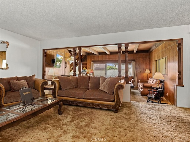 living area featuring carpet floors, wood walls, a textured ceiling, and beamed ceiling