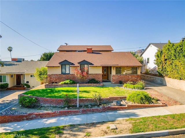 view of front of home featuring a shingled roof, a front yard, brick siding, and stucco siding