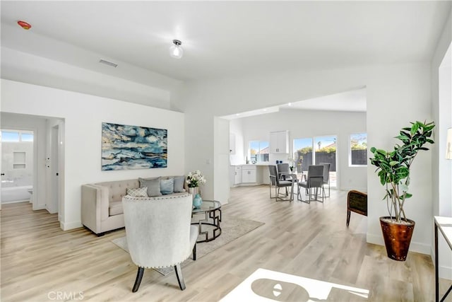 living area with vaulted ceiling, visible vents, light wood-style flooring, and baseboards