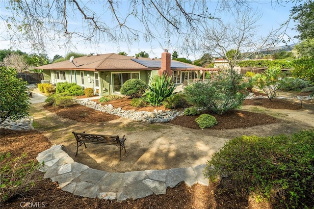 rear view of property featuring fence, a chimney, and solar panels