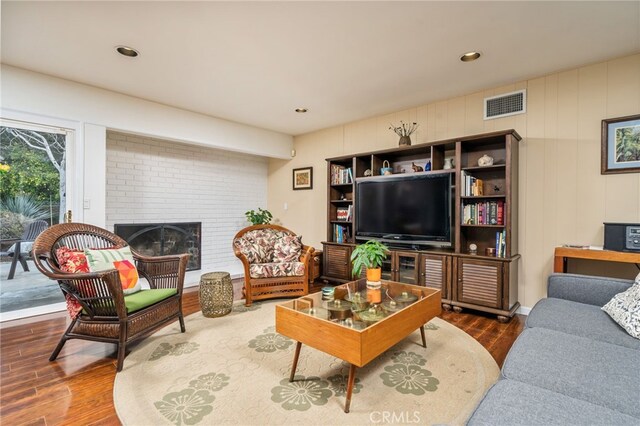 living area featuring a brick fireplace, visible vents, and wood finished floors