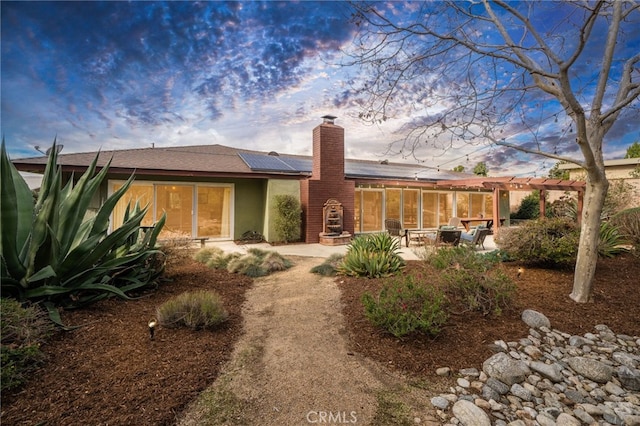 rear view of house with stucco siding, a patio, a chimney, and solar panels