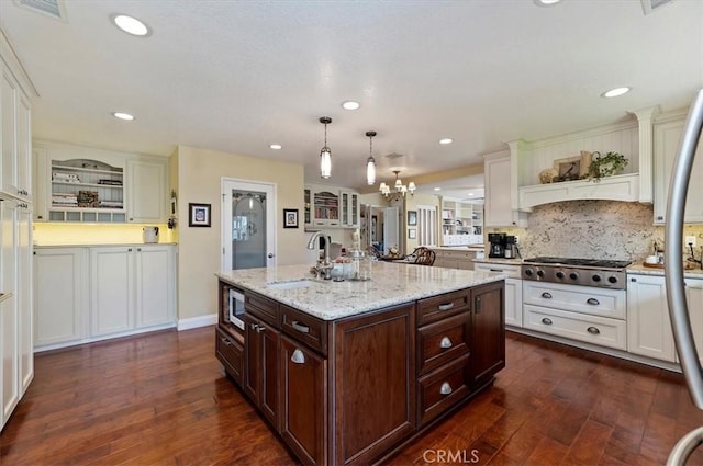 kitchen featuring dark brown cabinetry, a center island with sink, decorative light fixtures, open shelves, and a sink