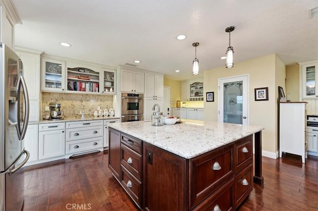 kitchen with open shelves, stainless steel appliances, hanging light fixtures, glass insert cabinets, and a kitchen island with sink