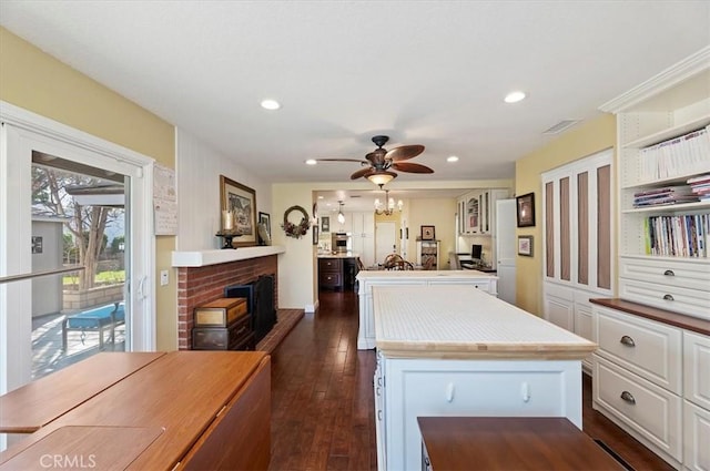 kitchen with dark wood finished floors, light countertops, a brick fireplace, white cabinets, and a kitchen island