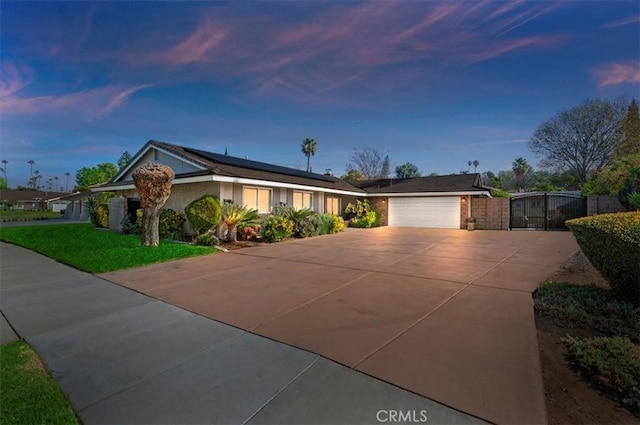 ranch-style home with a garage, solar panels, a yard, concrete driveway, and a gate