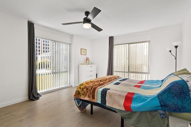 bedroom featuring a ceiling fan, multiple windows, baseboards, and wood finished floors