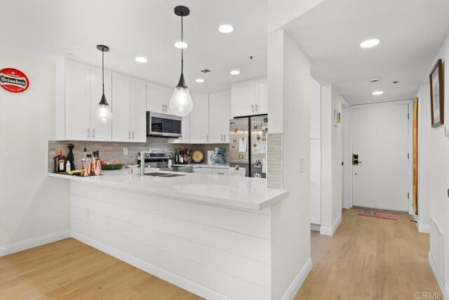kitchen with stainless steel appliances, a sink, a peninsula, white cabinets, and light wood-style flooring