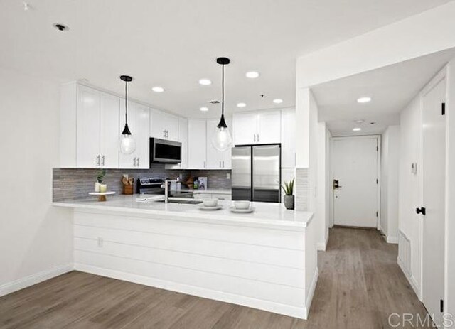 kitchen featuring appliances with stainless steel finishes, a peninsula, light countertops, backsplash, and wood finished floors