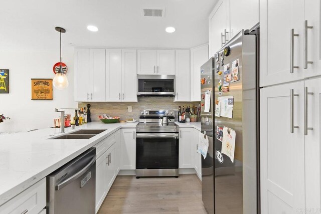 kitchen with appliances with stainless steel finishes, a sink, white cabinets, light wood-type flooring, and recessed lighting