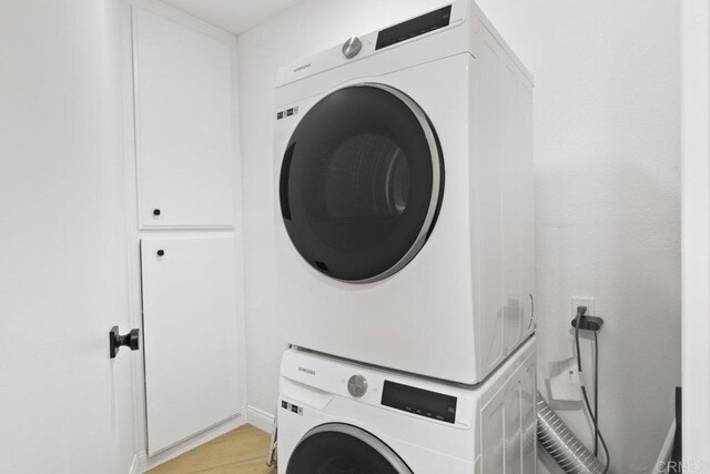clothes washing area with stacked washer and clothes dryer and light wood finished floors