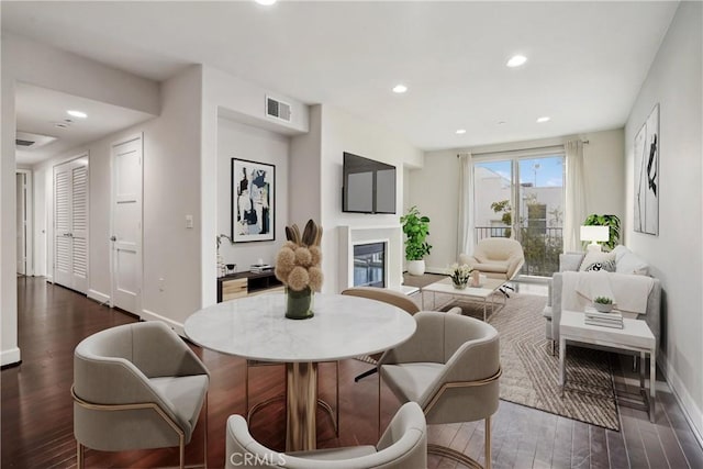 interior space with dark wood finished floors, a glass covered fireplace, visible vents, and recessed lighting