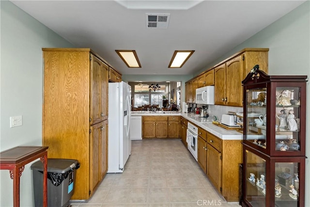 kitchen with brown cabinets, light countertops, visible vents, decorative backsplash, and white appliances