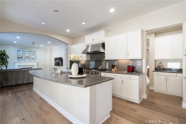 kitchen with arched walkways, a sink, dark countertops, light wood-style floors, and under cabinet range hood